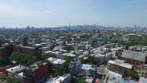 aerial of Brooklyn neighborhood with Manhattan skyline in background during day - rising shot
