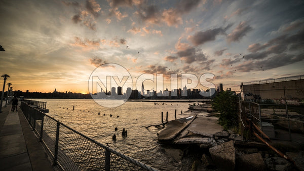 Manhattan skyline view from Brooklyn with birds flying in sky and wood dowels in East River water at sunset