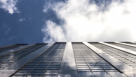 upward angle of single tall skyscraper in Manhattan during the day - 4K timelapse with clouds flying by overhead on blue sky