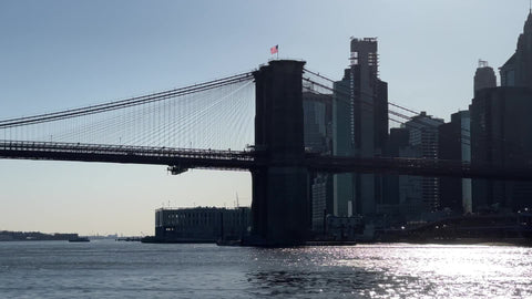 cars crossing Brooklyn Bridge over East River American flag waving in sky Downtown Manhattan New York City NYC