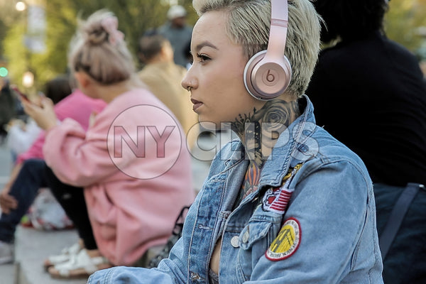 girl with tattoos listening to music on headphones in park