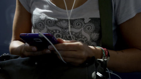tilting up from smartphone to woman on earbuds listing to music with gritty window view of graffiti on Queens buildings from elevated subway train