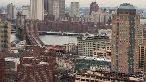 panning across Manhattan and Brooklyn Bridge with cars crossing in fast speed - time-lapse on East River water with buildings on cloudy day