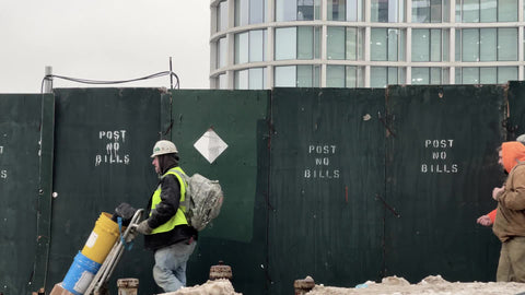 construction workers walking past site with post no bills painted sign on boarded up perimeter in New York City NYC