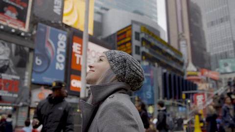 happy tourist looking around in Times Square smiling on cold winter day - pretty girl with hat and ads in 4K slow motion - contact us for model details
