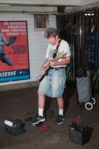 musician in shorts playing electric guitar in Manhattan subway station in summer