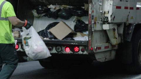 garbage man tossing trash into back of truck in slow motion on summer day in NYC