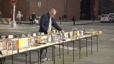 man selling books at vendor table on street