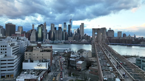 aerial toward Manhattan skyline alongside Brooklyn Bridge cars driving in NYC