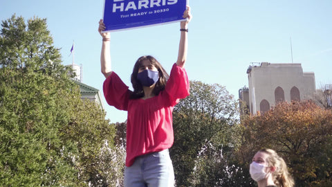 young woman holding up Biden Harris sign in Washington Square Park New York City