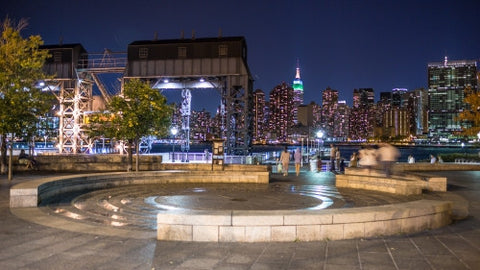 Manhattan skyline at night view from Long Island City circle stone benches and fountain in LIC