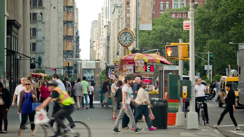 people walking on 5th Avenue in summer on sunny day with cars driving by, clock in background