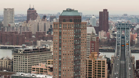 zooming out from Manhattan and Brooklyn Bridges - cars speeding across bridge in timelapse over East River with buildings on cloudy day