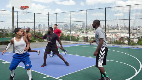 kids in competitive basketball game on outdoor courts with view of Manhattan skyline through fence