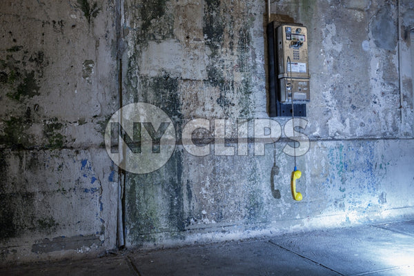 dangling public pay phone off the hook against dirty gritty wall in Brooklyn subway station