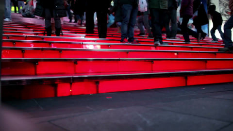 woman with high heels walking up famous red steps in Times Square at night