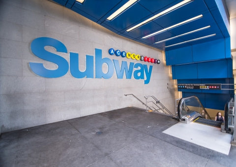 big blue subway sign off Times Square with stairs and escalator down
