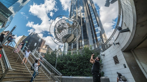 Columbus Circle with tourist photographer taking photo - famous globe sculpture and Trump Tower and people in Midtown Manhattan on sunny summer day from subway station stairs in NYC