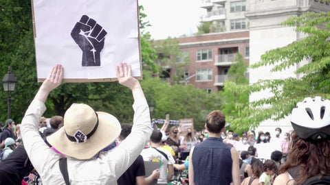 White woman holding Black fist logo on sign at BLM protest in Washington Square Park NYC