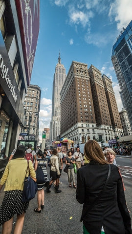 Empire State Building towering over 34th street and Herald Square on crowded busy street on summer day in Manhattan