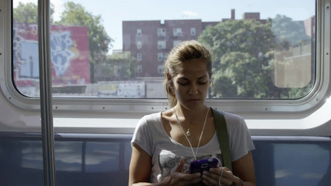 gritty neighborhood in Queens with graffiti on buildings passing in window background - woman listening to music on headphones