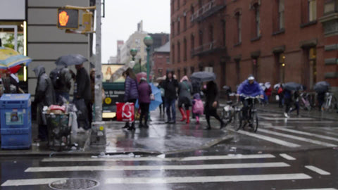 rainy day in SoHo - raining on people with umbrellas on Broadway and Prince street - man on bicycle in slow motion
