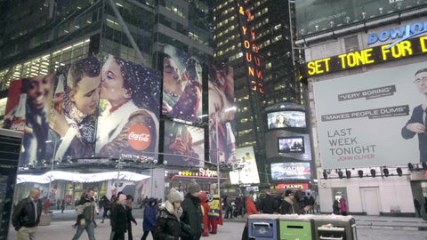 snowing Times Square with ticker, ads, and tourists walking at night - bright lights and signs in winter