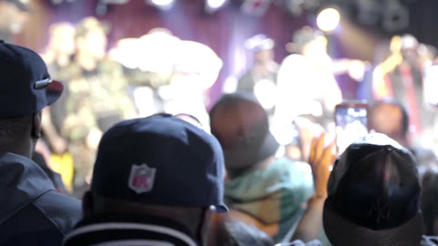 man in NFL cap on cell phone watching hip hop show from audience - crowd at rap show - live concert with bright lights on stage