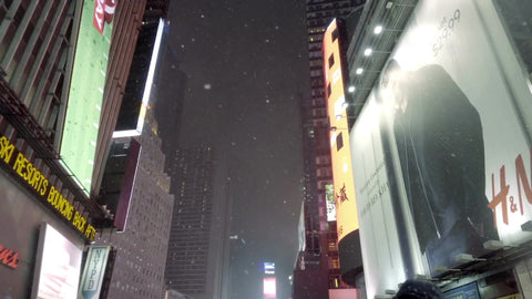 tilting down from night sky and bright billboards, ads in Times Square - snowing in slow motion