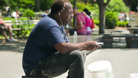 man sitting and enjoying music - listening to earbuds on summer day in Washington Square Park in New York City