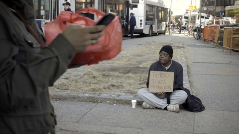 homeless African-American man with thyroid illness holding sign sitting on street, pedestrian putting change in his cup on cold fall winter day in NYC slow motion