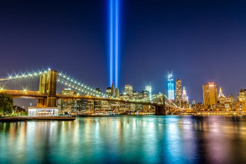 East River with 911 beams and Brooklyn Bridge reflecting off water, Manhattan skyline in background at night