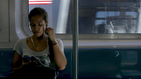 beautiful woman listening to music on subway - elevated train with graffiti buildings in Queens passing in background