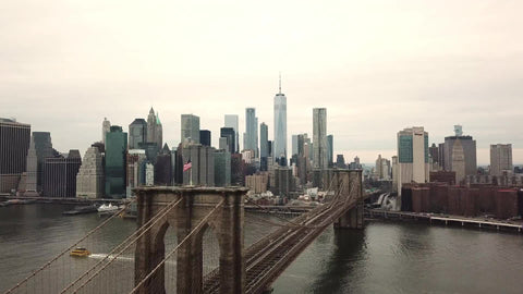 aerial flying over Brooklyn Bridge with American flag toward Manhattan skyline with Freedom Tower and skyscrapers in 4K and 1080 HD