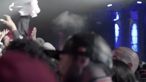 rap fans at show in audience watching performers on stage in slow motion under bright smoky lights
