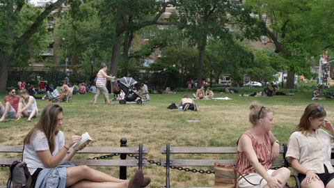 tracking shot of girl reading on bench and people sitting in grass in Washington Square Park - 4K slow motion in NYC