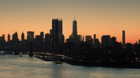 panning across Downtown Manhattan skyline Brooklyn Bridge sulhouette of buildings on East River water at sunset New York City NYC