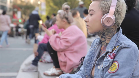 young woman with tattoos listening to headphones in park