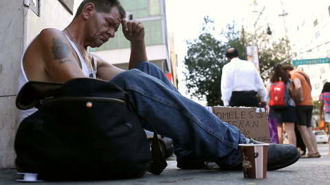 low view of homeless white veteran man sitting on sidewalk with sign and cup in Union Square Manhattan New York City