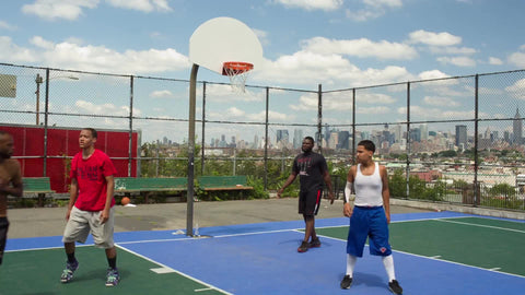 man scores jump shot in pickup game on outdoor basketball courts with view of Manhattan skyline in NYC