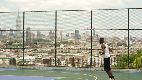 slam dunk - man slamming basketball with both hands off backboard - dunking with Empire State Building view through fence on summer day