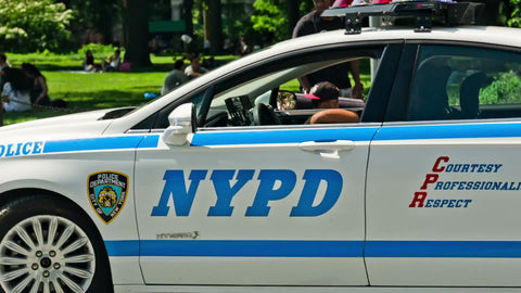NYPD police car driving through Washington Square Park in summer on bright sunny day - NYC