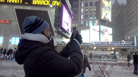 Middle-Eastern man taking video and pictures with smartphone in Times Square - snowing in winter at night