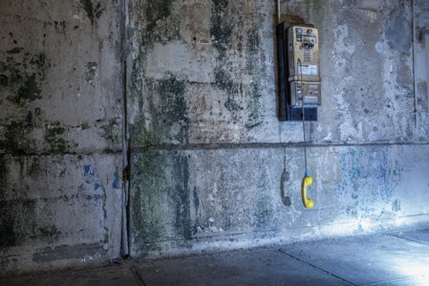 dangling public pay phone off the hook against dirty gritty wall in Brooklyn subway station