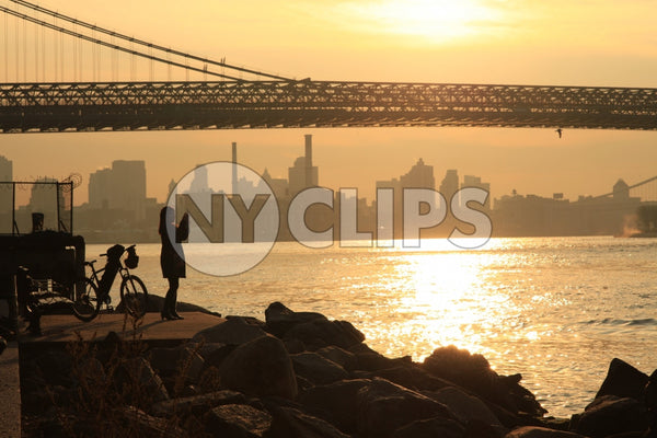 woman taking picture of Manhattan Bridge at sunset - beautiful orange sky over East River from Brooklyn