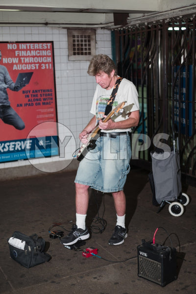 musician in shorts playing electric guitar in Manhattan subway station in summer