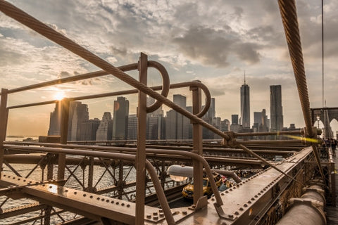 steel beams of Brooklyn Bridge close-up with Manhattan skyline in background at sunset in NYC