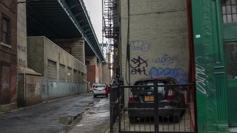 driving past empty desolate alley with car driving down street with puddles - gritty graffiti and woman walking by in Chinatown on wet fall day