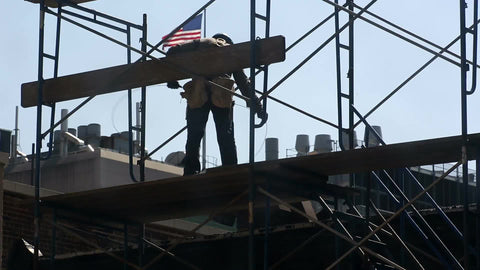 construction worker on scaffolding - man in hardhat with American flag in background in New York City