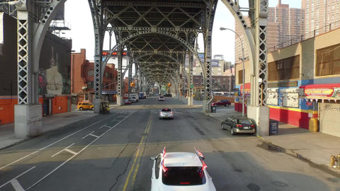 street in Harlem with cars driving under elevated subway train track on sunny day in NYC
